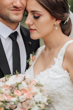 Bir gelin ve damat bir buket çiçekli fotoğraf için poz veriyorlar. Gelin beyaz bir elbise giyiyor ve damat bir takım elbise giyiyor. Sahne mutlu ve romantik.