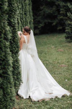 Beyaz elbisesi ve duvağı olan bir gelin tarlada duruyor. Elinde bir buket çiçek tutuyor.