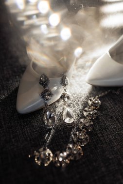 Üzerinde kolye ve küpe olan bir çift beyaz ayakkabı. Ayakkabılar siyah bir yüzeyde.