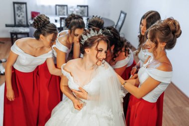 Bir gelin, tüm kırmızı elbiseler giyen nedimeleriyle çevrilidir. Gelin gülümsüyor ve anın tadını çıkarıyor.