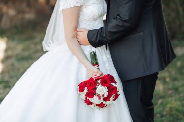 Bir gelin ve damat ellerinde bir buket kırmızı gülle birbirlerini kucaklıyorlar. Gelin beyaz bir elbise giyiyor ve damat siyah bir takım elbise giyiyor. Aşk ve mutluluk kavramı