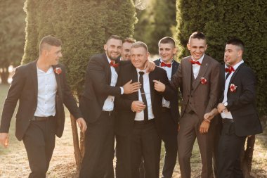 Takım elbiseli ve kravatlı bir grup adam fotoğraf için poz veriyor. Hepsi gülümsüyor ve birbirlerine sarılıyorlar. Sahne mutlu ve dostane.