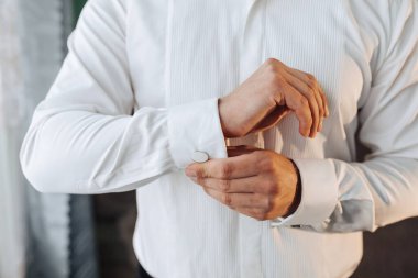 Bir adam beyaz gömlek giyiyor ve gömleğinin manşetini düzeltiyor. Formalite ve detaylara dikkat etme kavramı. Çünkü adam düzgün giyinmeye özen gösteriyor.