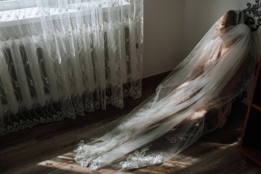 Kafasında bir peçeyle yerde oturan bir kadın. Oda loş bir şekilde aydınlandı ve kadın derin derin düşünüyor.