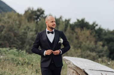 Siyah takım elbiseli ve beyaz kravatlı bir adam tarlada duruyor. Yakasına beyaz bir çiçek takıyor. Zarafet ve entelektüellik anlayışı, çünkü adam resmi giyinmiş.