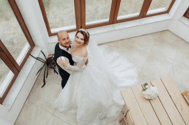 Bir adam ve bir kadın üzerinde vazo olan bir masanın önünde duruyorlar. Kadın gelinlik giyiyor ve erkek de takım elbise giyiyor. Sahne mutlu ve kutlama dolu.