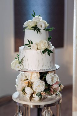 Üzerinde çiçekler olan beyaz bir pasta. Pasta beyaz çiçeklerle süslenmiş ve gümüş bir tabanı var.