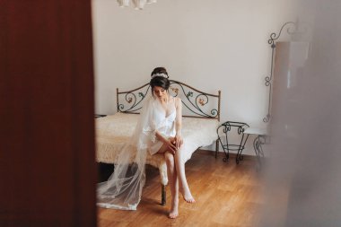 Beyaz elbiseli bir kadın yatağa oturur. Duvak ve taç takıyor.