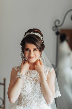 Bir kadın gelinlik ve taç giyiyor. Gülümsüyor ve kameraya bakıyor.