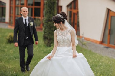 Bir gelin ve damat çimenli bir alanda birlikte yürüyorlar. Gelin beyaz bir elbise ve duvak takıyor.