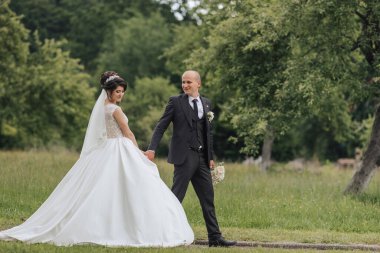 Bir gelin ve damat bir tarlada birlikte yürüyorlar. Gelin beyaz bir elbise giyiyor ve damat da takım elbise giyiyor.