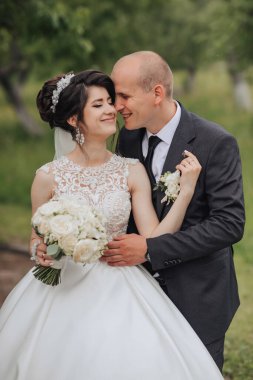 Gelin ve damat bir tarlada duruyorlar, gelin bir buket tutuyor ve damat kravat takıyor.