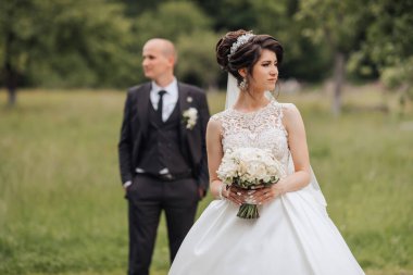 Gelin ve damat bir buket ve peçeyle bir tarlada dururlar.