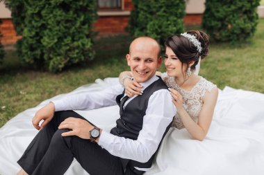 Bir adam ve bir kadın çimenli bir alanda battaniyenin üzerinde oturuyorlar. Adam saat takıyor ve kadın gelinlik giyiyor. Gülümsüyorlar ve birbirlerinin arkadaşlığından zevk alıyor gibiler.