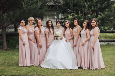 Pembe elbiseli bir grup kadın fotoğraf için poz veriyor. Kadınlardan biri beyaz bir elbise giyiyor ve saçına çiçek takıyor.