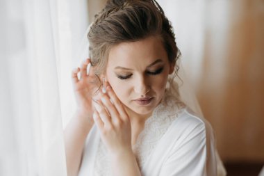 Bir kadın düğüne hazırlanıyor, makyajını yapıyor ve saçını düzeltiyor. Beyaz bir elbise ve duvak takıyor.