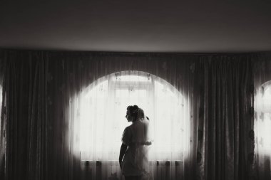 Gelinlikli bir kadın pencerenin önünde duruyor. Oda loş bir şekilde aydınlatılmış ve görünen tek kişi kadın. Sahne kasvetli ve samimi, çünkü odada yalnız bir kadın var.