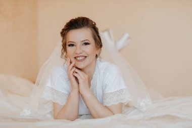 Kafasında beyaz bir peçe olan bir kadın yatakta yatıyor. Gülümsüyor ve mutlu.