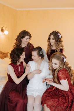 Beş kadından oluşan bir grup bir yatakta oturuyor ve içlerinden biri gelinlik giyiyor. Manzara sıcak ve dostça, kadınlar bir araya toplanmış ve birbirlerinin arkadaşlığından keyif alıyorlar.