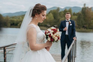 Gelin ve damat gelinin elinde bir buket çiçekle iskelede dururlar.