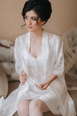 Beyaz elbiseli bir kadın kanepede oturuyor. Dantelli bir bluz ve beyaz bir bornoz giyiyor.