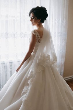 Beyaz elbiseli bir kadın pencerenin önünde duruyor. Peçe ve küpe takıyor.