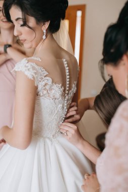 Beyaz elbiseli bir kadın düğüne hazırlanıyor. Bir kadın elbisesini ayarlamasına yardım ediyor.