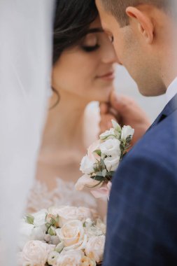 Bir gelin ve damat aralarında bir buket çiçekle birbirlerine sarılıyorlar. Gelin beyaz bir elbise giyiyor ve damat mavi bir takım elbise giyiyor. Aşk ve mutluluk kavramı