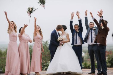 Bir grup insan, gelin ve damadın ortasında olduğu bir düğünü kutluyorlar. Gelin beyaz bir elbise giyiyor ve damat bir takım elbise giyiyor. Grup bir tepede duruyor.