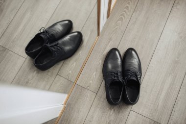 İki siyah ayakkabı bir aynanın önünde duruyor. Ayakkabılar siyah ve parlak ve ikisi de bağlı. Aynadaki ayakkabıların yansıması bir simetri ve denge hissi yaratır.