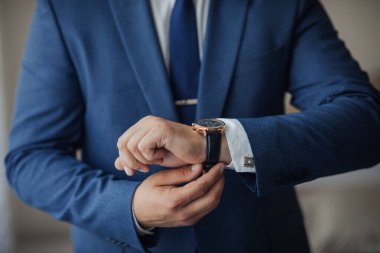 Mavi takım elbiseli ve kravatlı bir adam saatini kontrol ediyor. Formalite ve profesyonellik kavramı. Çünkü adam takım elbise ve kravat giymiş.