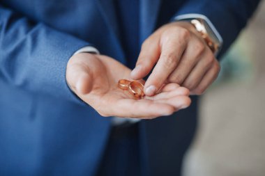 Bir adam elinde iki altın alyans tutuyor. Yüzükler parmaklarına takıldı ve mavi bir takım elbise giyiyor. Aşk ve bağlılık kavramı, adamın ortağına evlenme teklif etmek üzere olduğu gibi.