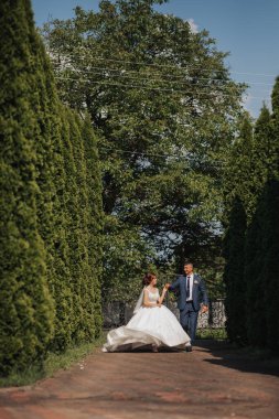 Bir gelin ve damat bahçede bir patikada yürüyorlar. Gelin beyaz bir elbise giyiyor ve damat mavi bir takım elbise giyiyor. Çift gülümsüyor ve o mutlu. Bahçe ağaçlarla dolu.