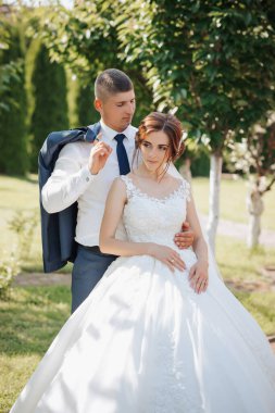 Bir gelin ve damat parkta fotoğraf için poz veriyorlar. Gelin beyaz bir elbise giyiyor ve damat mavi bir takım elbise giyiyor. Sahne mutlu ve romantik.