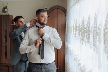 İki adam giyiniyor, biri kravat takıyor. Diğer adam izlerken kravatlı adam ayarlama yapıyor. Sahne penceresi olan bir odada geçiyor ve duvarda bir saat var.