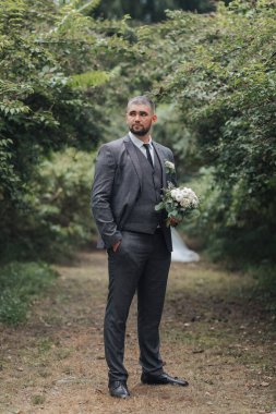 Takım elbiseli ve kravatlı bir adam bir buket çiçekle ormanda duruyor. Zarafet ve entelektüellik kavramı. Çünkü adam resmi giyinmiş ve elinde güzel bir buket tutuyor.