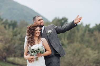 Gelin ve damat bir tarlada duruyorlar, damat gökyüzünü işaret ediyor. Gelin bir buket tutuyor ve damat bir takım elbise giyiyor. Sahne mutlu ve kutlama dolu.