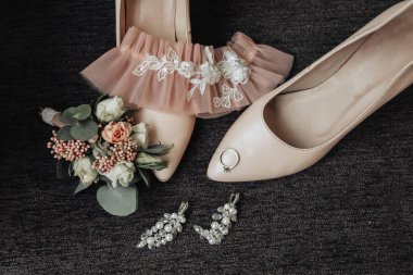 Yan tarafında pembe dantelli ve ayak parmağında yüzük olan bir çift ayakkabı. Ayakkabıların yanına bir buket çiçek konur.