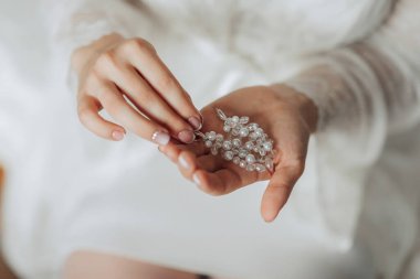 Bir kadın elinde bir kolye tutuyor. Kolye berrak boncuklardan yapılmış ve çok parlak. Kadın beyaz bir bornoz giyiyor ve bir sandalyede oturuyor. Zarafet ve incelik kavramı