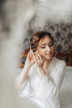Bir kadın düğüne hazırlanıyor, duvağını takıyor ve saçını düzeltiyor. İmajın yumuşak, romantik bir havası var. Gelin güzel ve büyük gün için hazır görünüyor.