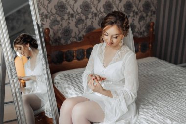 Bir kadın bir yatakta oturuyor ve aynadaki yansımasına bakıyor. O, beyaz bir elbise giyiyor ve ellerini birbirine kenetledi. Zarafet ve incelik kavramı