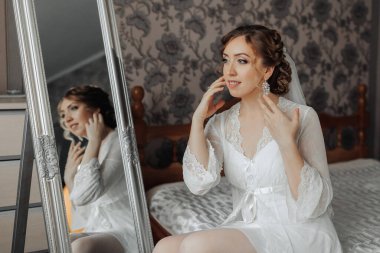 Bir kadın yatakta oturuyor ve aynada kendine bakıyor. Beyaz bir önlük giyiyor ve saçları topuz şeklinde. Zarafet ve incelik kavramı