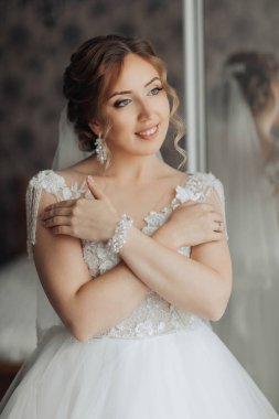 Gelinlik giymiş bir kadın fotoğraf için poz veriyor. İnci bir bilezik ve peçe takıyor.