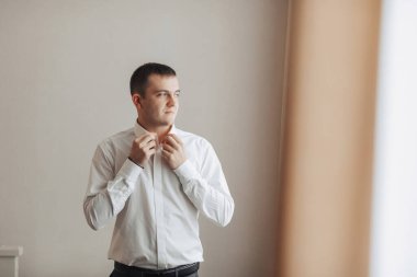 Beyaz gömlekli bir adam pencerenin önünde giyiniyor. Rutin ve günlük hayat kavramı, adam sabahları giyinirken...