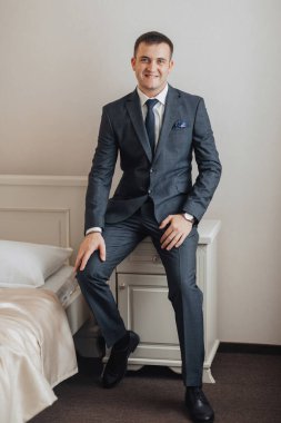 Takım elbiseli bir adam yatakta oturuyor. Gülümsüyor ve kravat takıyor. Güven ve profesyonellik kavramı