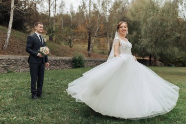 Bir gelin ve damat çimen tarlasında duruyor. Gelin beyaz bir elbise giyiyor ve damat bir takım elbise giyiyor. Gelin bir buket tutuyor ve damat da bir buket tutuyor.