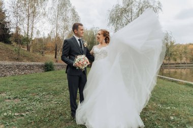 Gelin ve damat çimenli bir tarlada duruyorlar, gelinin elbisesi arkasında akıyor.