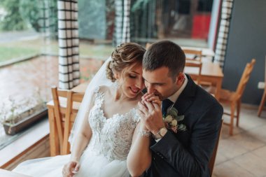 Bir gelin ve damat restoranda bir masada oturuyor, el ele tutuşuyor ve gülümsüyor. Sahne mutlu ve romantik.