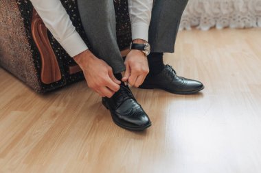 Bir adam ayakkabılarını giyiyor. O bir saat takıyor ve bir sandalyede oturuyor.