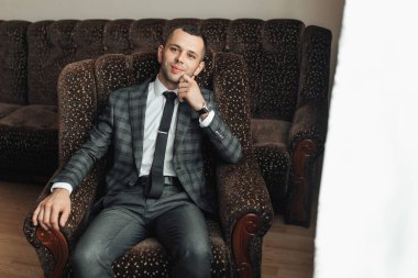 Takım elbiseli ve kravatlı bir adam sandalyede oturuyor. Gülümsüyor ve rahatladı.